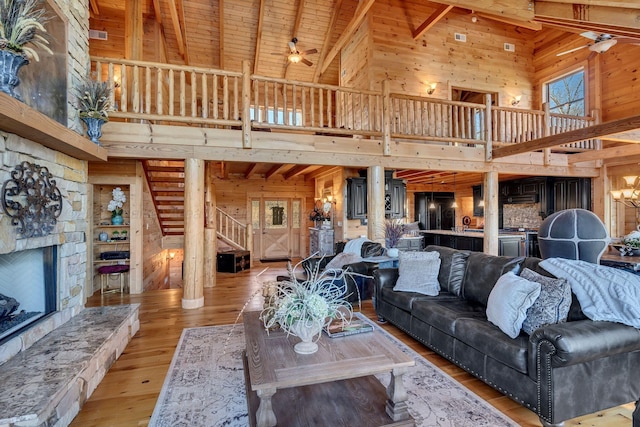 living area featuring a high ceiling, wooden walls, a ceiling fan, a fireplace, and stairs