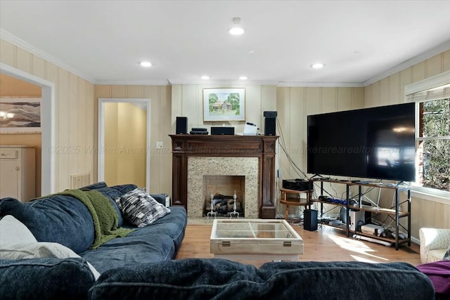 living room with a premium fireplace, recessed lighting, ornamental molding, visible vents, and wood finished floors