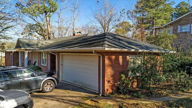 view of side of home featuring aphalt driveway, an attached garage, a chimney, and brick siding