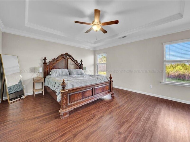 bedroom with visible vents, crown molding, baseboards, wood finished floors, and a raised ceiling