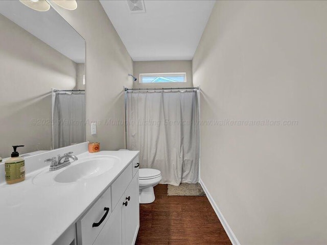 full bathroom with toilet, vanity, wood finished floors, baseboards, and visible vents