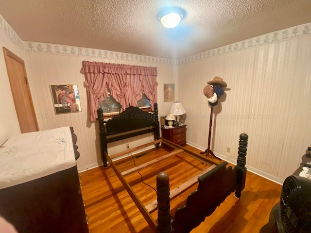 bedroom featuring a textured ceiling, baseboards, and wood finished floors