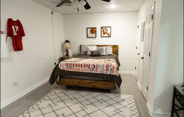 bedroom with hardwood / wood-style floors, ceiling fan, and a drop ceiling