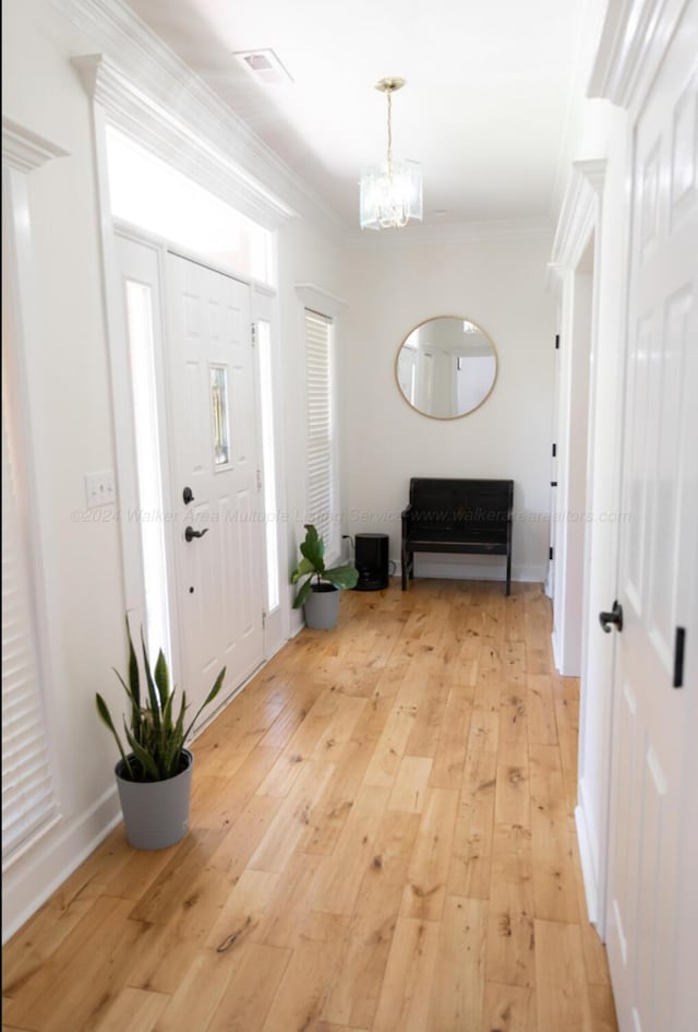 foyer entrance with ornamental molding, a notable chandelier, and light wood-type flooring