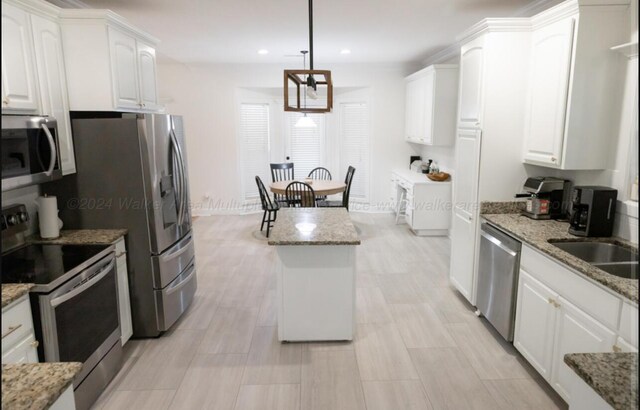 kitchen featuring light stone counters, white cabinetry, stainless steel appliances, and hanging light fixtures