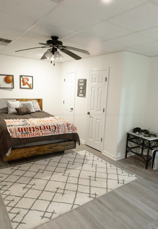 bedroom with light wood-type flooring, a drop ceiling, and ceiling fan