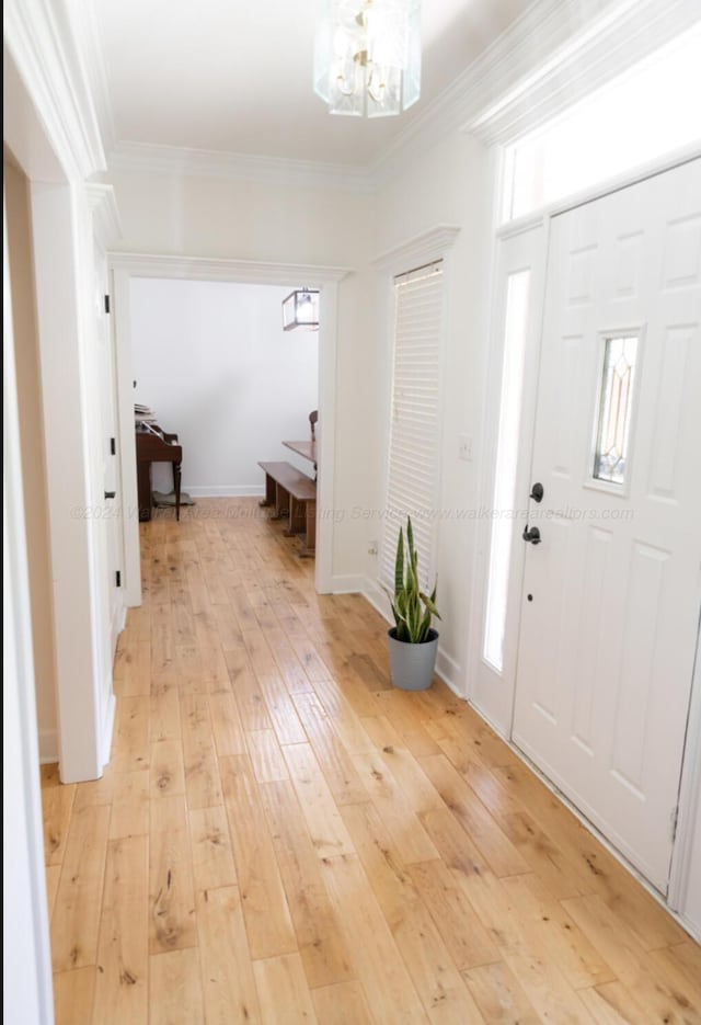 entrance foyer with crown molding, light hardwood / wood-style flooring, and a notable chandelier