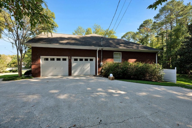 view of home's exterior featuring brick siding, driveway, fence, and an attached garage