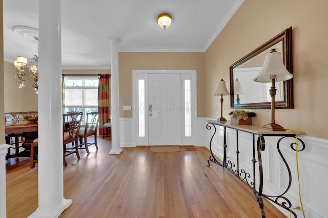 foyer entrance with decorative columns, a wainscoted wall, ornamental molding, and light wood-style floors