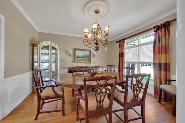 dining room with a wainscoted wall, a notable chandelier, crown molding, and light wood-style floors