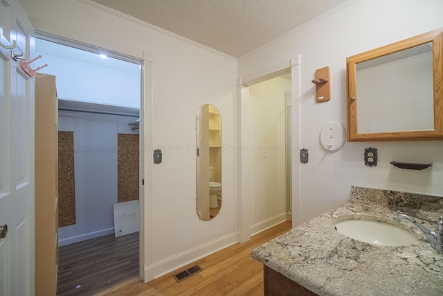 bathroom featuring a textured ceiling, visible vents, ornamental molding, toilet, and wood finished floors