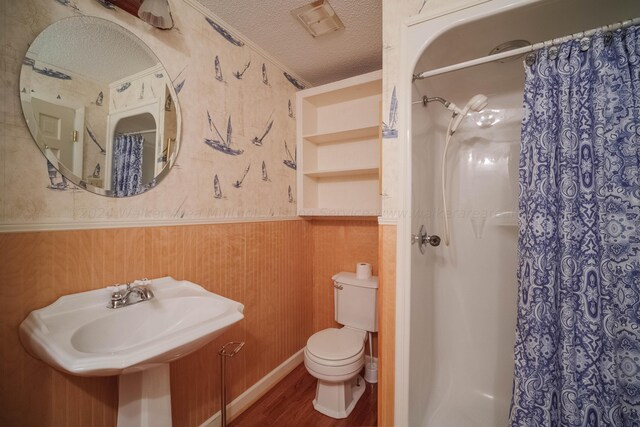 bathroom with wood finished floors, toilet, a shower with shower curtain, a textured ceiling, and wainscoting