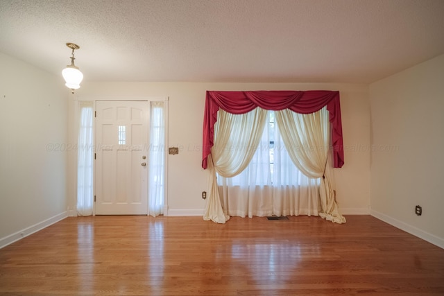 foyer entrance featuring visible vents, baseboards, light wood finished floors, and a textured ceiling