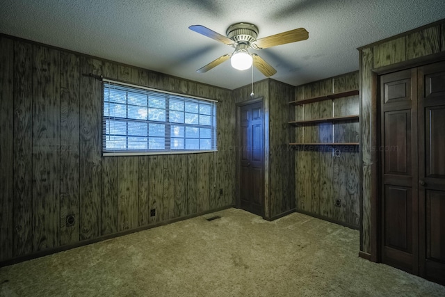 carpeted spare room with visible vents, a ceiling fan, wooden walls, and a textured ceiling