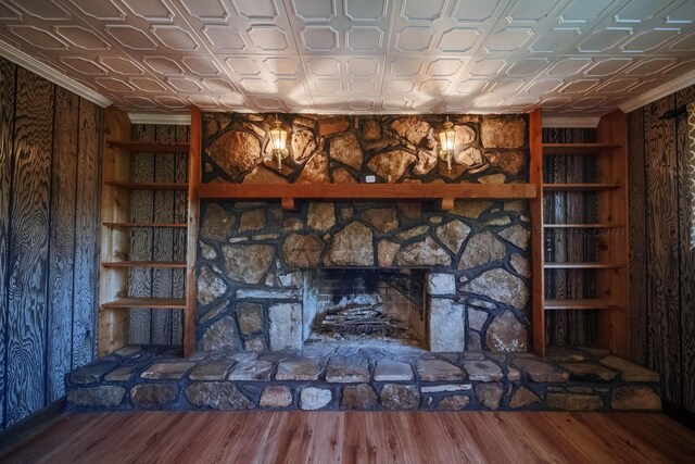 interior details with a notable chandelier, an ornate ceiling, built in shelves, a stone fireplace, and wood finished floors