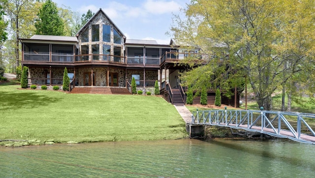 back of property with a yard, a deck with water view, stairs, and a sunroom