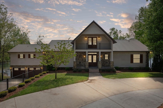 view of front of house featuring a yard, fence, a garage, french doors, and a balcony
