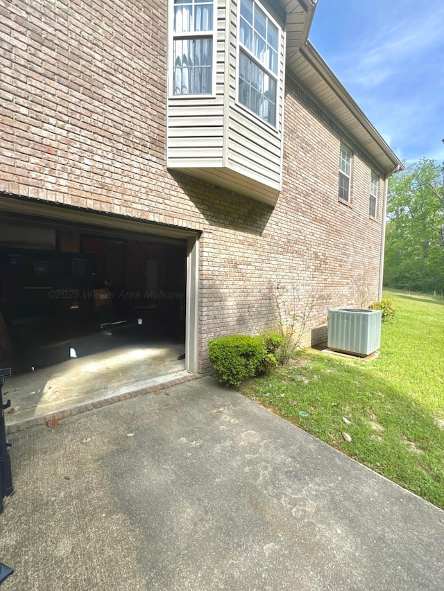 view of property exterior featuring a lawn, aphalt driveway, brick siding, and central air condition unit
