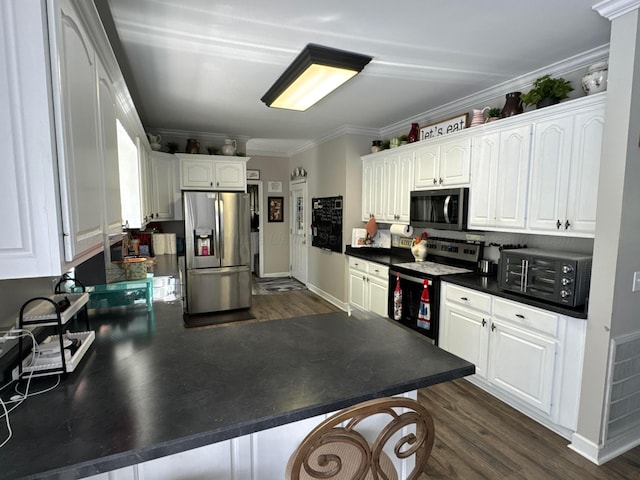 kitchen featuring dark wood finished floors, stainless steel appliances, dark countertops, a peninsula, and white cabinetry