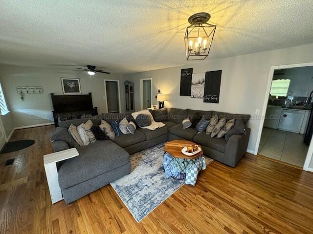 living room featuring ceiling fan with notable chandelier, plenty of natural light, hardwood / wood-style floors, and a textured ceiling