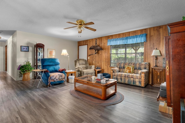 living area with wood walls, wood finished floors, baseboards, a textured ceiling, and ceiling fan