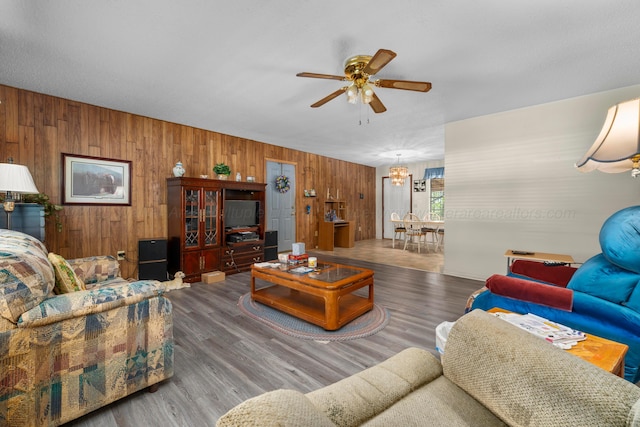 living area with wooden walls, wood finished floors, and ceiling fan with notable chandelier