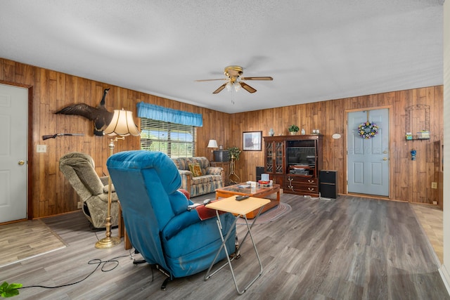 living area featuring wooden walls, wood finished floors, and ceiling fan