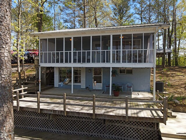 rear view of property featuring metal roof, central air condition unit, a wooden deck, and a sunroom