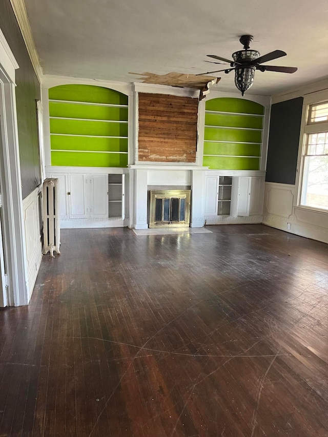 unfurnished living room with a ceiling fan, a decorative wall, a glass covered fireplace, and built in shelves