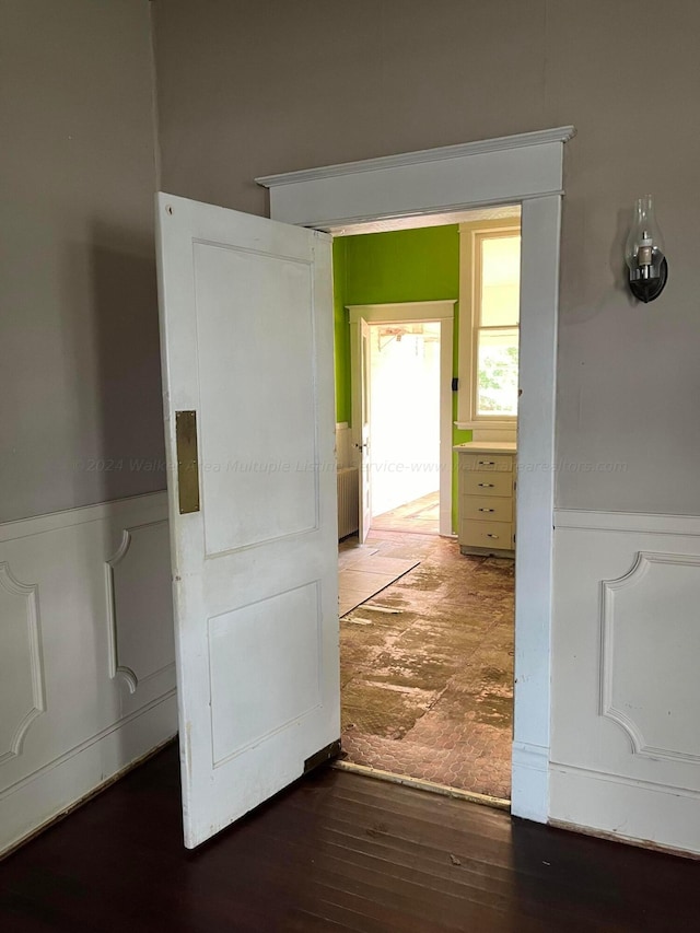 hall featuring radiator heating unit, wainscoting, a decorative wall, and wood finished floors