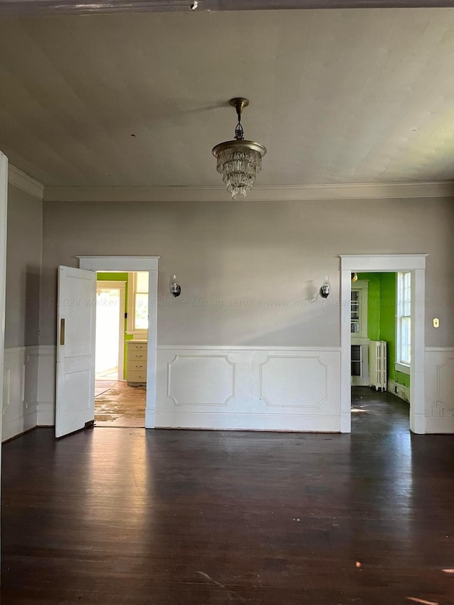 empty room featuring ornamental molding, wood finished floors, wainscoting, and radiator