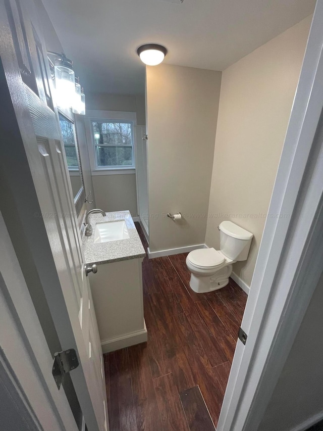bathroom featuring baseboards, wood finished floors, toilet, and vanity