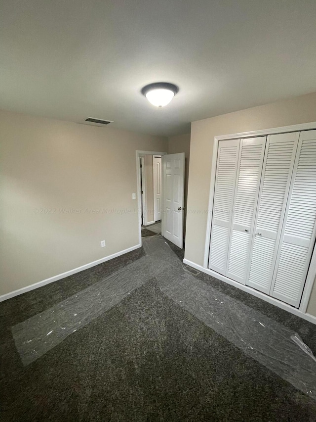 unfurnished bedroom with baseboards, visible vents, a closet, and dark colored carpet