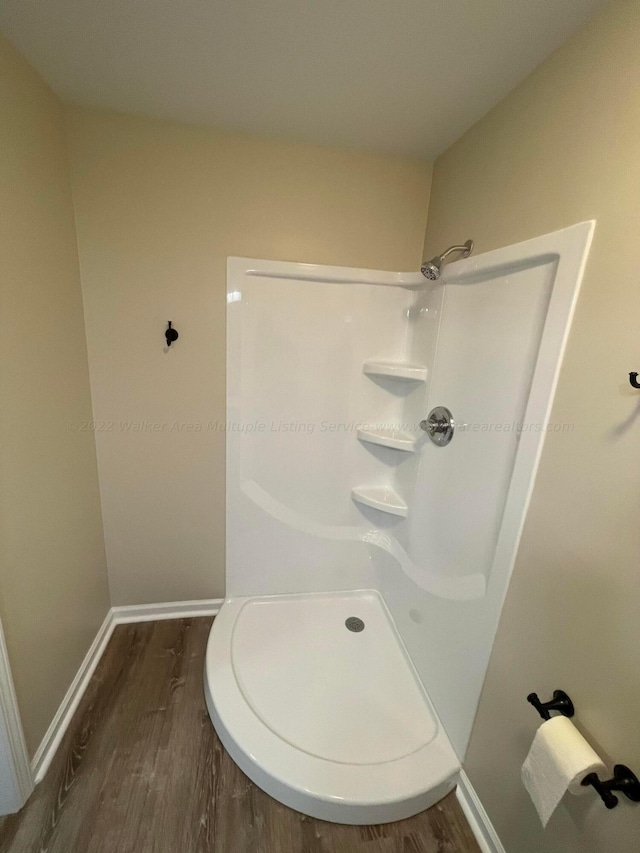 bathroom featuring wood finished floors, baseboards, and walk in shower