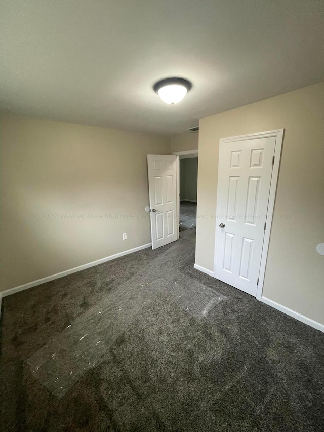 unfurnished bedroom with baseboards, visible vents, and dark colored carpet