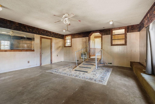 basement featuring a textured ceiling, ceiling fan, and wood walls