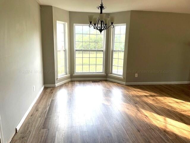 unfurnished dining area featuring baseboards, an inviting chandelier, and dark wood-style floors