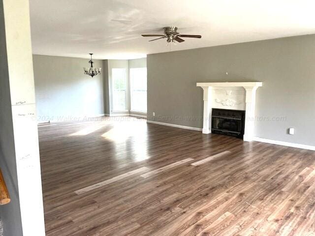 unfurnished living room with baseboards, wood finished floors, ceiling fan with notable chandelier, and a fireplace