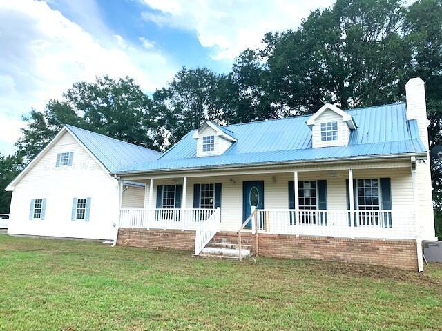 view of front of house with covered porch, a chimney, metal roof, and a front lawn