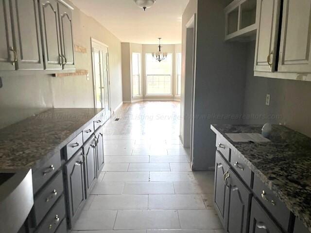 kitchen with gray cabinets, dark stone countertops, and a chandelier