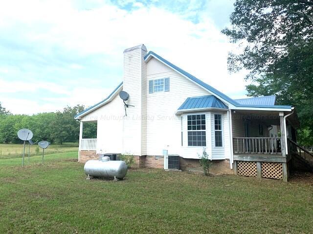 back of property with a yard, covered porch, a chimney, and metal roof