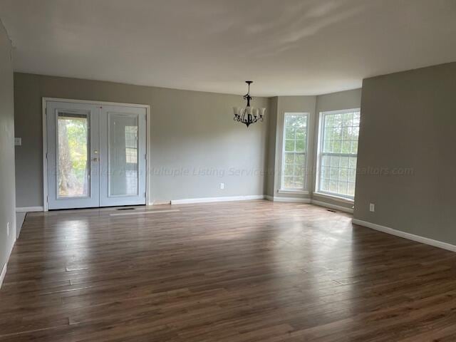 unfurnished room with plenty of natural light, baseboards, a notable chandelier, and dark wood finished floors