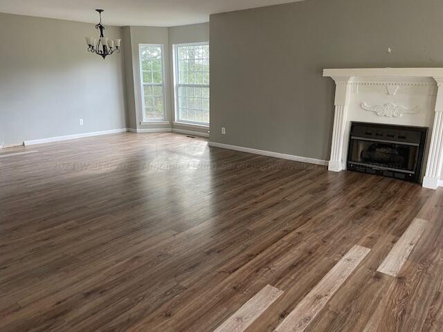 unfurnished living room with an inviting chandelier, baseboards, a fireplace, and dark wood-type flooring