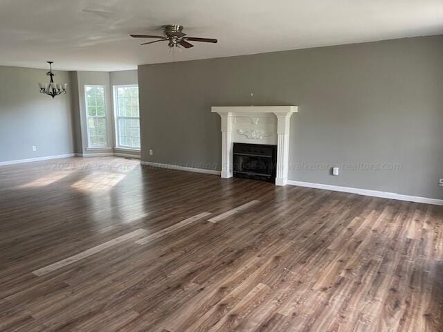 unfurnished living room with baseboards, dark wood finished floors, ceiling fan with notable chandelier, and a fireplace