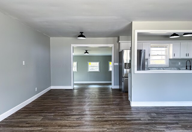 kitchen with white cabinets, stainless steel fridge, baseboards, a sink, and dark wood-style floors