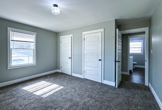 unfurnished bedroom featuring baseboards, two closets, and dark colored carpet