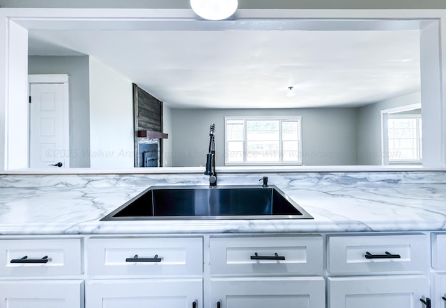 kitchen with white cabinetry, a sink, and light stone countertops