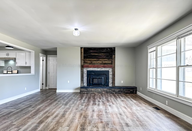 unfurnished living room with baseboards, visible vents, a fireplace, and wood finished floors