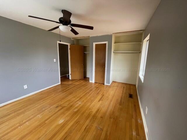 unfurnished bedroom with wood finished floors, multiple closets, baseboards, visible vents, and ceiling fan