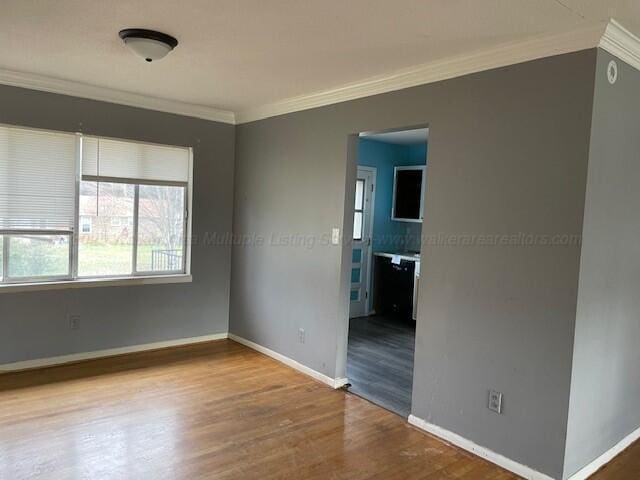 empty room featuring baseboards, wood finished floors, and crown molding